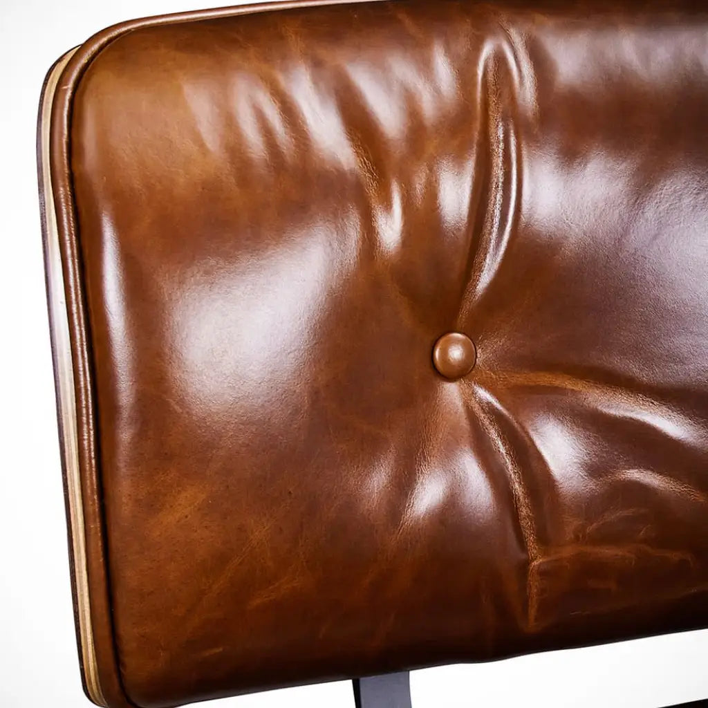 Close-up of a brown leather upholstered chair or cushion with tufted button detailing and visible grain texture against a white background.